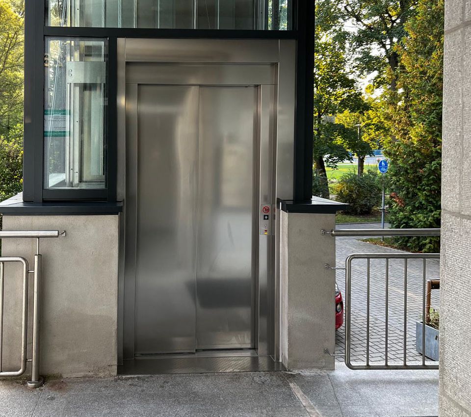 Edelstahlt&uuml;r des Aufzugs in einem verglasten Aufzugsschacht.