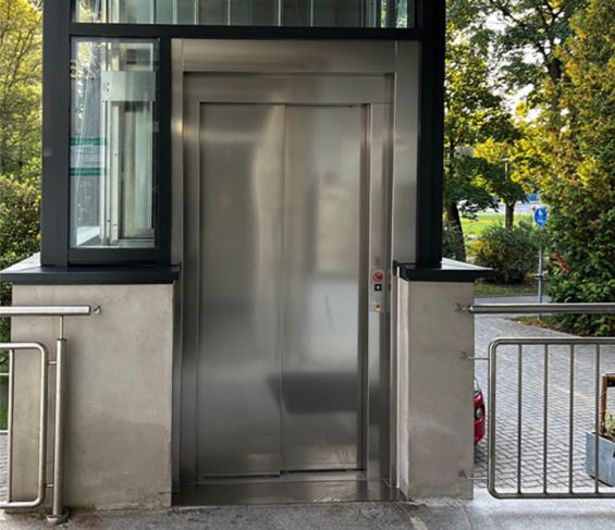 Edelstahlt&uuml;r des Aufzugs in einem verglasten Aufzugsschacht.